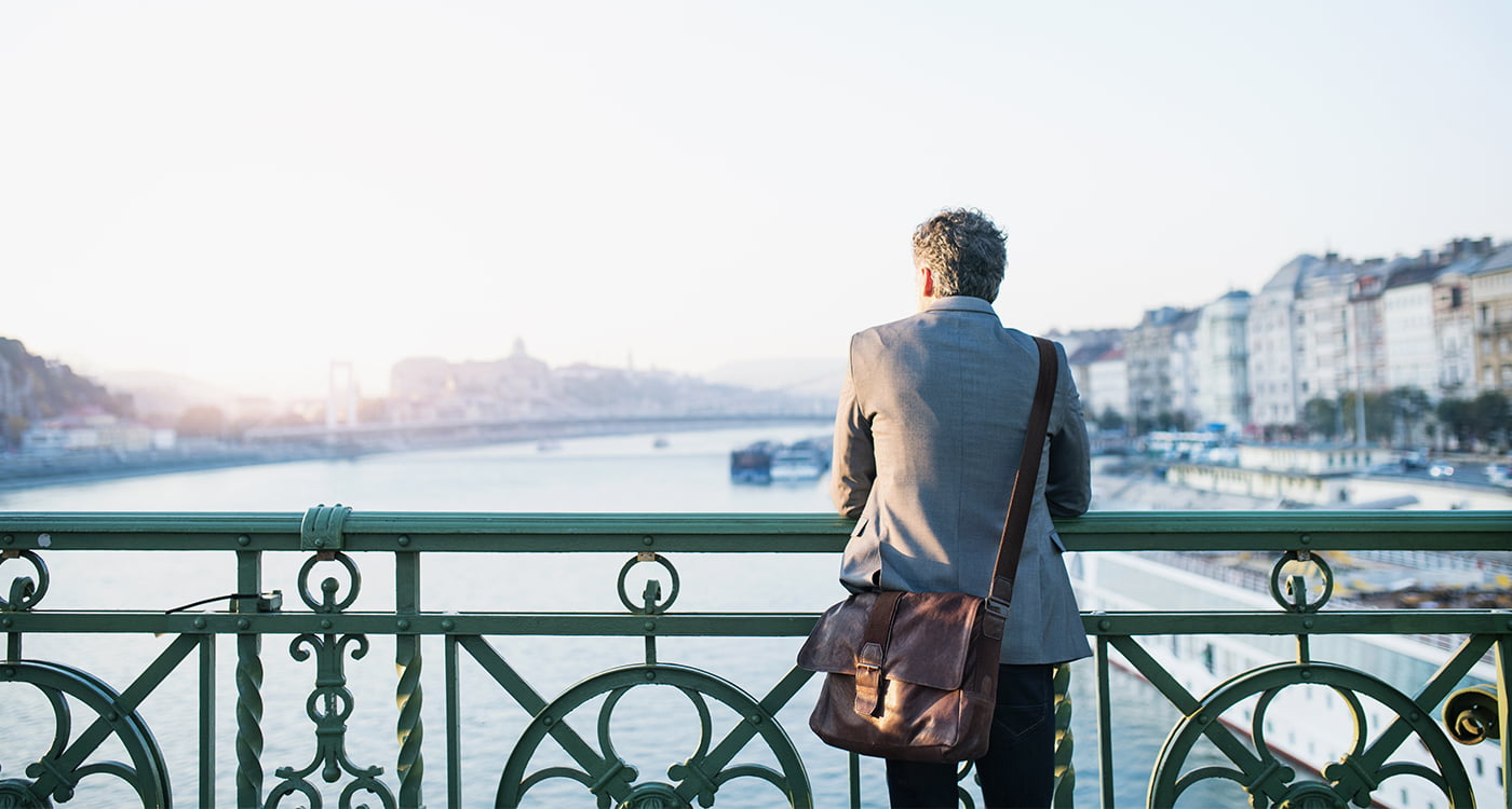 man facing away leaning on a fence looking out into the water